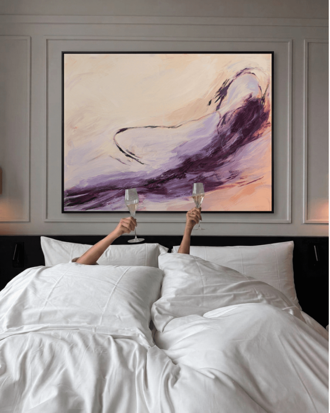 Champagne flutes raised in front of an original painting above a hotel bed